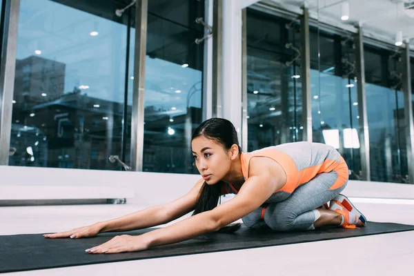 Attractive asian girl stretching hands on fitness mat at gym — Stock Photo