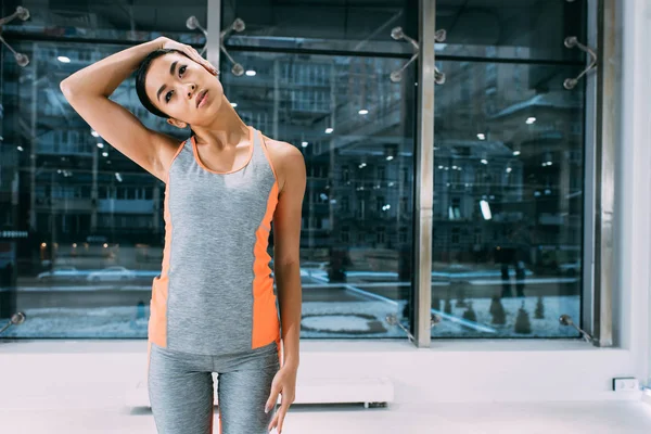 Тонка азіатська дівчина стоїть і розтягує шию в спортзалі — стокове фото
