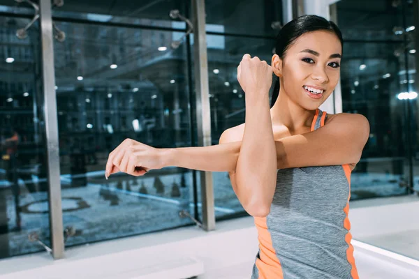 Close up view of smiling asian girl stretching hand and looking at camera at gym — Stock Photo