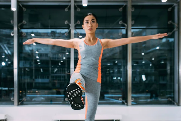 Slim asian girl standing on one leg at gym — Stock Photo