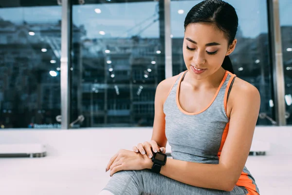 Smiling asian girl looking at camera fitness tracker at gym — Stock Photo