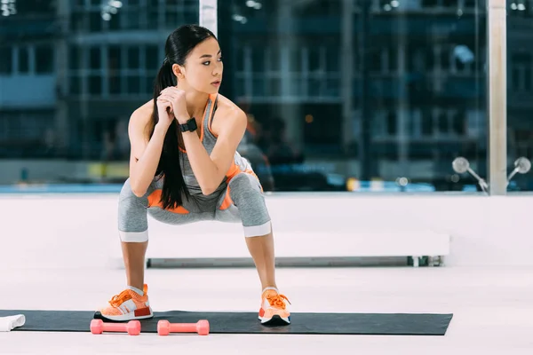 Привлекательная азиатская девушка делает приседания на фитнес-мат в тренажерном зале — стоковое фото