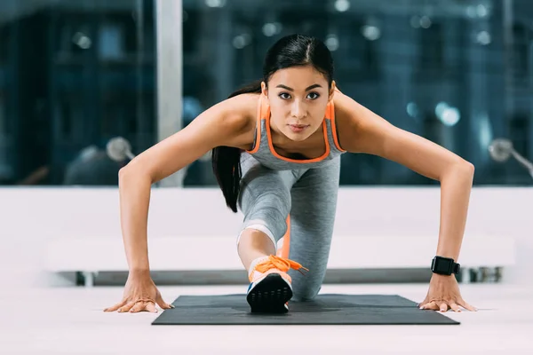 Athletic asian sportswoman stretching leg on fitness mat in sports center — Stock Photo