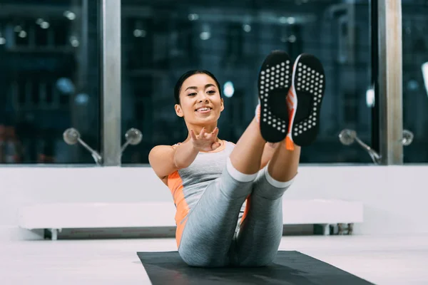 Beautiful asian sportswoman smiling and training on fitness mat in sports center — Stock Photo