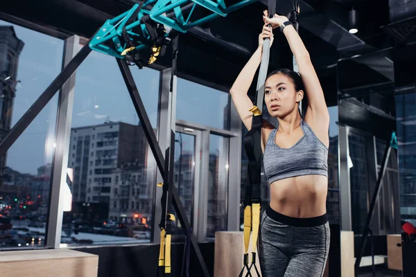 Slim asian girl in sportswear training with resistance bands at modern gym — Stock Photo