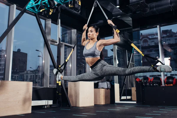 Athletic asian sportswoman doing split with resistance bands in fitness center — Stock Photo