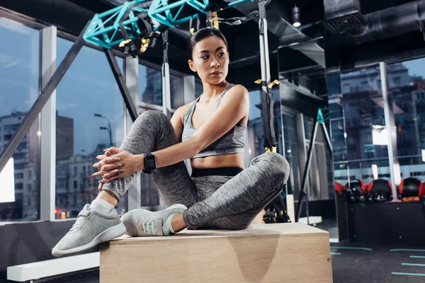 Attractive asian girl sitting on wooden cube at gym — Stock Photo