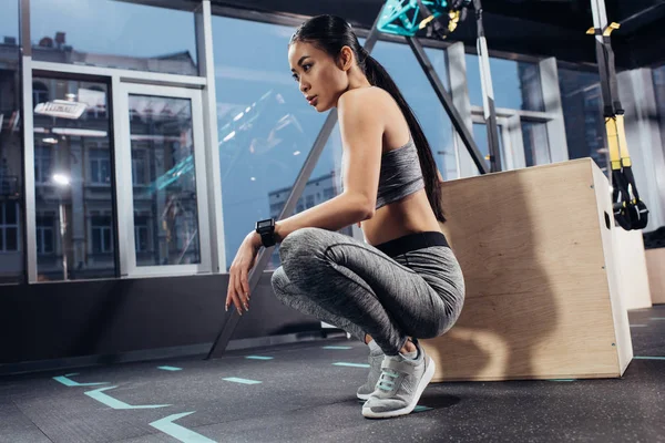 Attractive asian girl sitting near big wooden cube at gym — Stock Photo