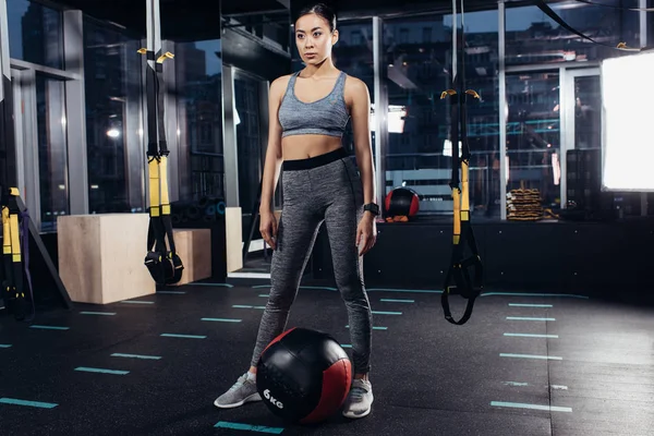 Slim asian girl standing near medicine ball at gym — Stock Photo