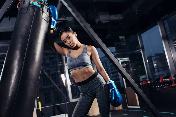 Sexy asiatique fille dans boxe gants debout près poinçon sac à gym — Photo de stock