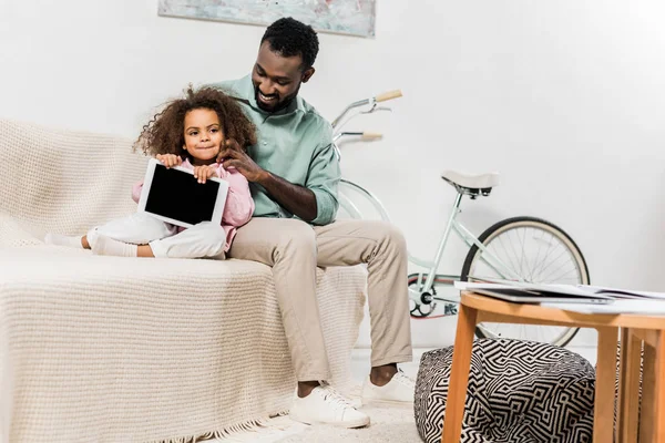 African american father and daughter using digital tablet and sitting on couch — Stock Photo