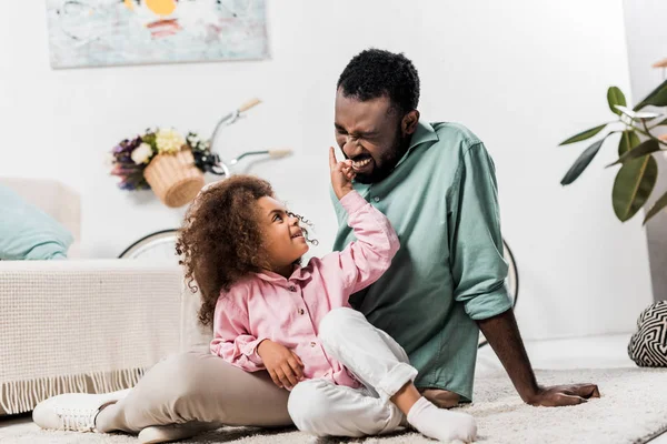 Smiling african american family sitting on rug and playing with each other — Stock Photo
