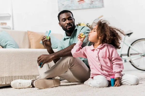 African american family sitting on floor and blowing soap bubbles — Stock Photo