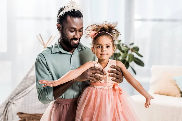 Glücklich lächelnd afrikanisch-amerikanischer Vater hebt schöne Tochter in rosa Kleid hoch — Stockfoto