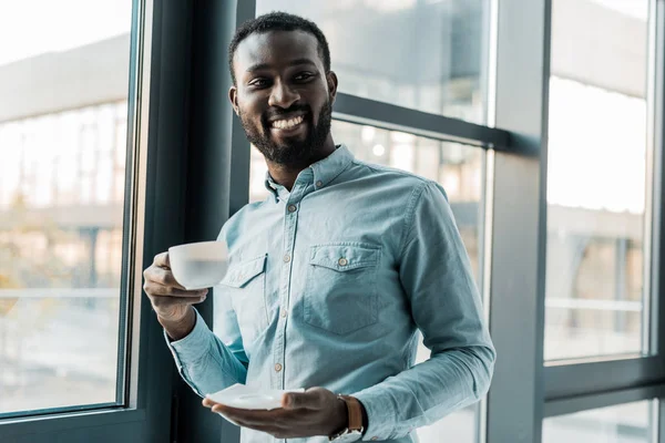 Africano americano hombre sosteniendo taza de café y mirando a la cámara - foto de stock