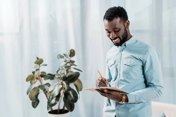 Smiling african american man writing in notepad — Stock Photo