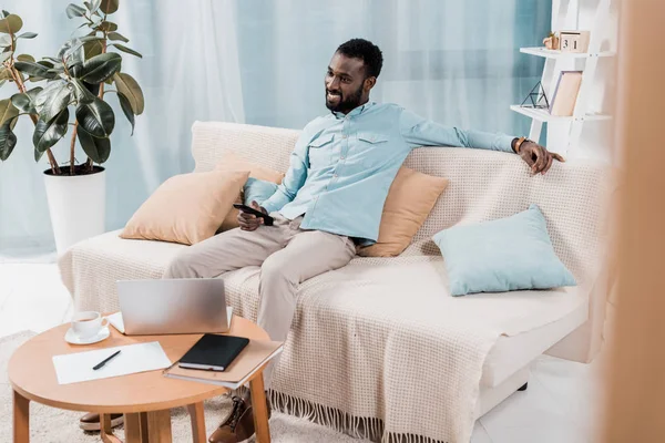 Uomo afroamericano che guarda la TV e si siede sul divano in soggiorno — Foto stock