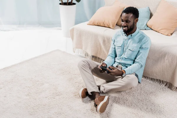 Homme afro-américain assis sur le sol et jouer au jeu vidéo dans le salon — Photo de stock