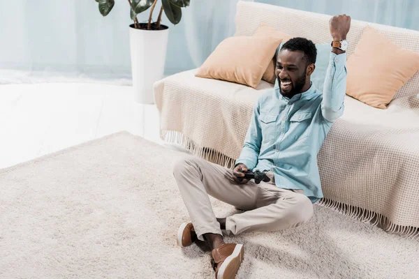 Afroamericano hombre jugando video y regocijo en sala de estar - foto de stock