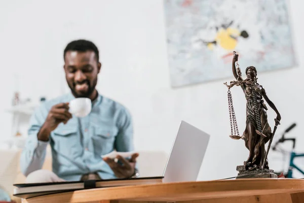 Selektiver Fokus der Gerechtigkeitsskala auf dem Tisch mit verschwommenem afrikanisch-amerikanischem Mann im Hintergrund — Stockfoto