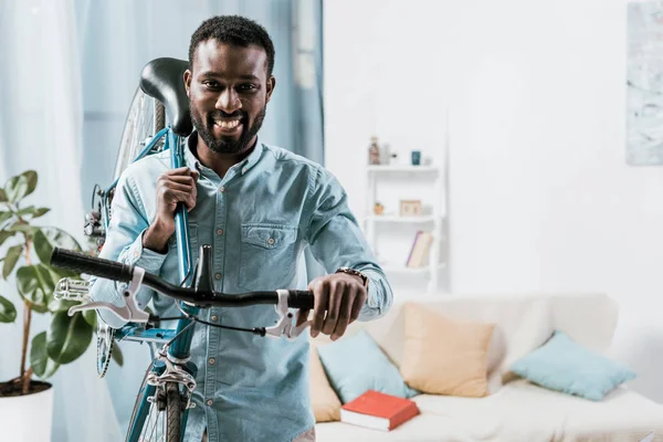 Афроамериканський чоловік носить велосипед і посміхається у вітальні — стокове фото