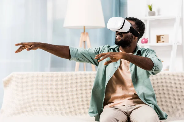 Hombre afroamericano usando auriculares de realidad virtual en la sala de estar - foto de stock