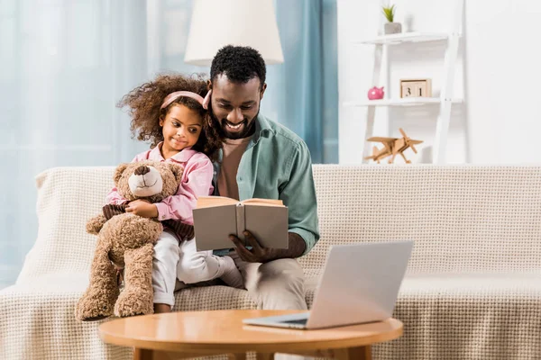 Hombre afroamericano leyendo con hija en sala de estar - foto de stock