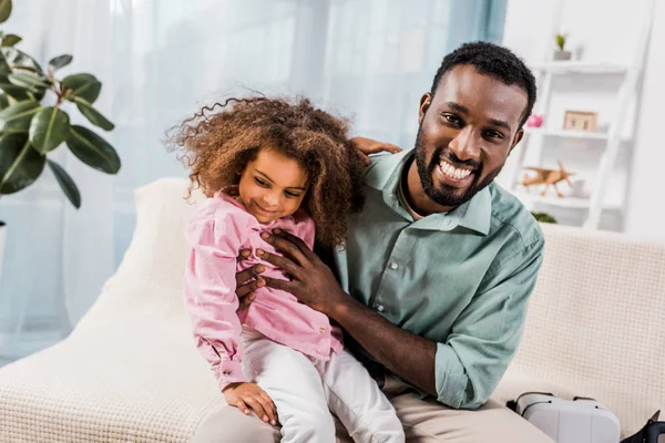 Père afro-américain tenant sa fille à genoux dans le salon — Photo de stock