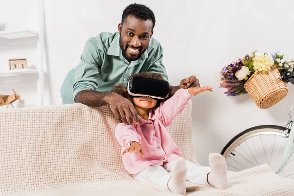 African american man showing daughter virtual reality glasses in living room — Stock Photo