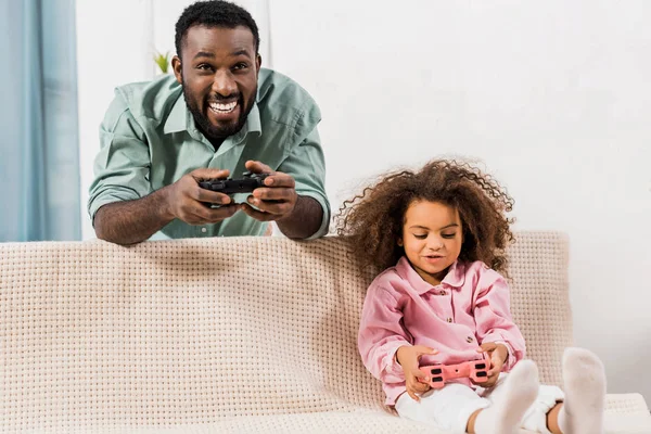 Afrikanisch-amerikanischer Vater steht und spielt Videospiel mit Tochter im Wohnzimmer — Stockfoto