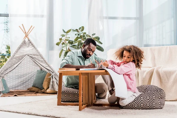 Afro-americano pai ajudando filha com desenho na sala de estar — Fotografia de Stock