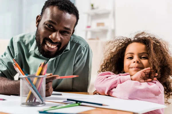 Vista da vicino del papà afro-americano che tiene la matita e aiuta la figlia con il disegno in soggiorno — Foto stock