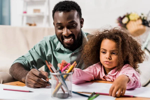 Primer plano vista de afroamericano papá ayudar hija con dibujo en sala de estar - foto de stock