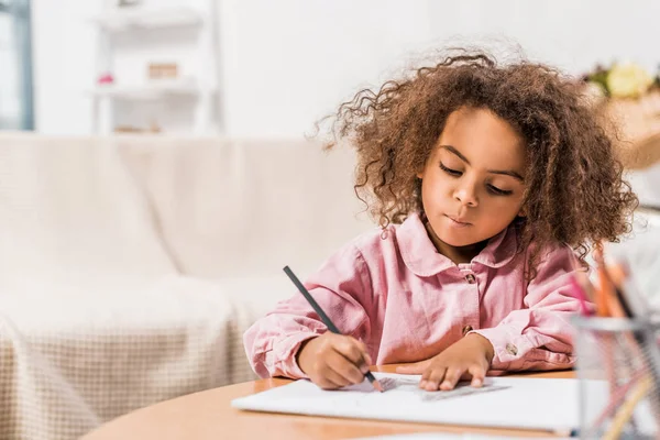 Niño afroamericano serio dibujo sobre papel con lápiz de color en la sala de estar - foto de stock