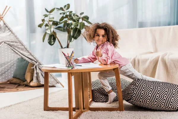 African american child drawing and showing thumb up in living room — Stock Photo