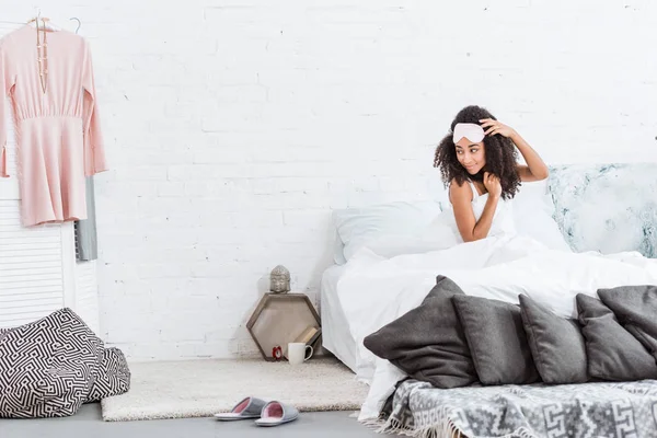 Selective focus of young african american woman with blindfold on forehead sitting in bed during morning time at home — Stock Photo