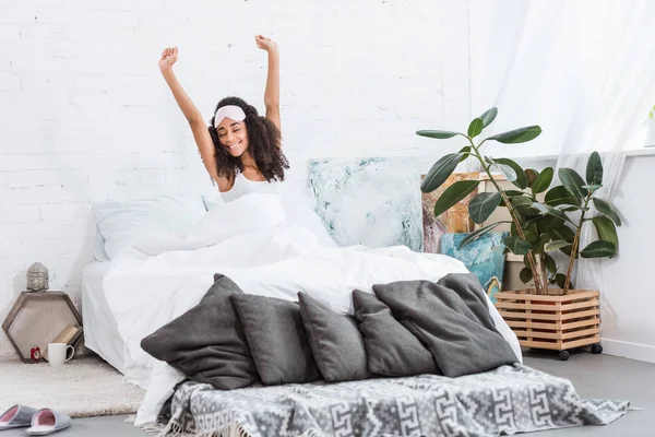 Jovem mulher americana africana alegre com venda na testa esticando na cama durante o tempo da manhã em casa — Fotografia de Stock