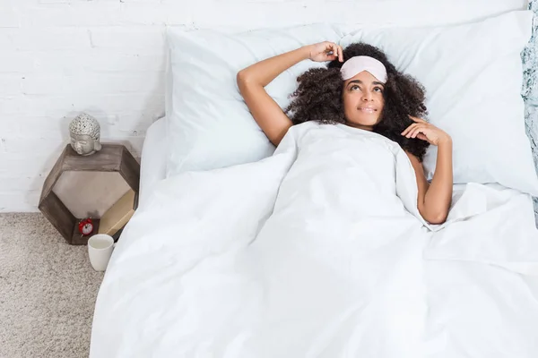 Hochwinkelaufnahme einer jungen afrikanisch-amerikanischen Frau mit Augenbinde auf der Stirn im Bett während der Morgenstunde zu Hause — Stockfoto