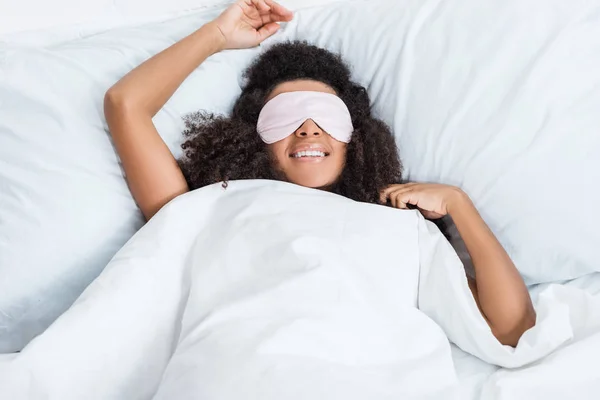 Alegre menina afro-americana com os olhos cobertos por olhos de dormir venda na cama durante o tempo da manhã em casa — Fotografia de Stock