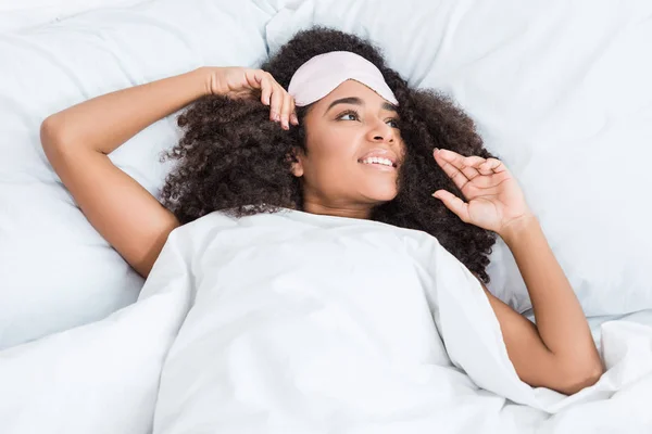 Jeune femme afro-américaine souriante avec les yeux bandés sur le front couché au lit pendant le matin à la maison — Photo de stock