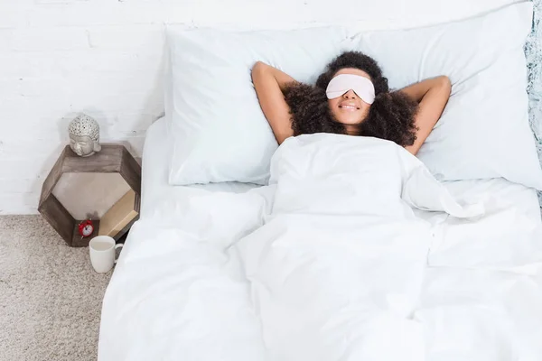 High angle view of african american girl with eyes covered by sleeping blindfold in bed during morning time at home — Stock Photo