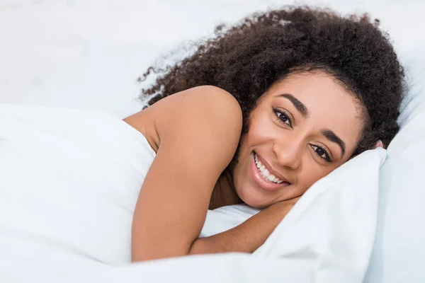 Glückliche junge afrikanisch-amerikanische Frau liegt im Bett und schaut in die Kamera — Stockfoto