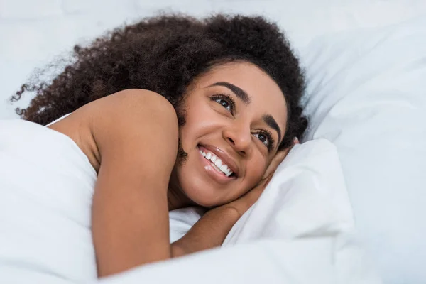 Glückliche junge afrikanisch-amerikanische Frau liegt im Bett und schaut in die Kamera — Stockfoto