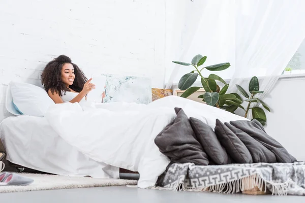 Foyer sélectif de la jeune femme afro-américaine en utilisant une tablette numérique au lit pendant la matinée à la maison — Photo de stock