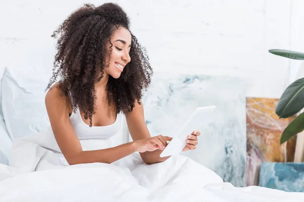 Happy african american young woman using digital tablet in bed during morning time at home — Stock Photo