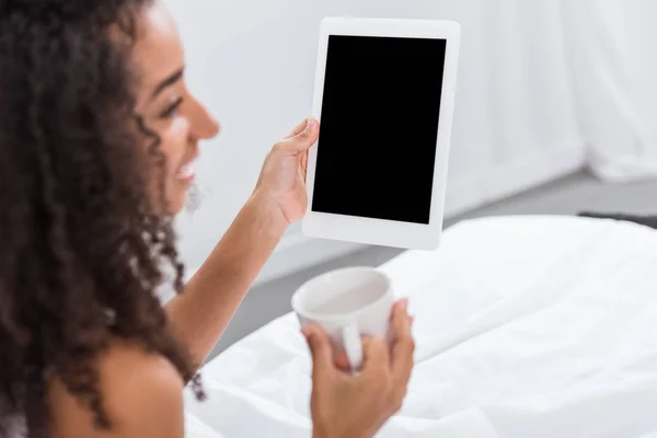 Foco seletivo da mulher afro-americana com xícara de café usando tablet digital na cama em casa — Fotografia de Stock