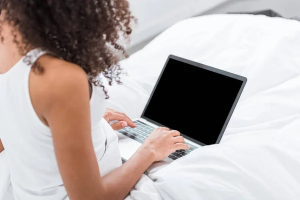 Partial view of curly girl using laptop with blank screen in bed during morning time at home — Stock Photo