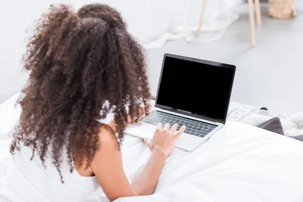 Rear view of curly girl using laptop with blank screen in bed during morning time at home — Stock Photo