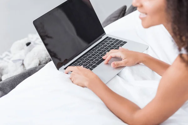 Partial view of woman using laptop with blank screen in bed during morning time at home — Stock Photo