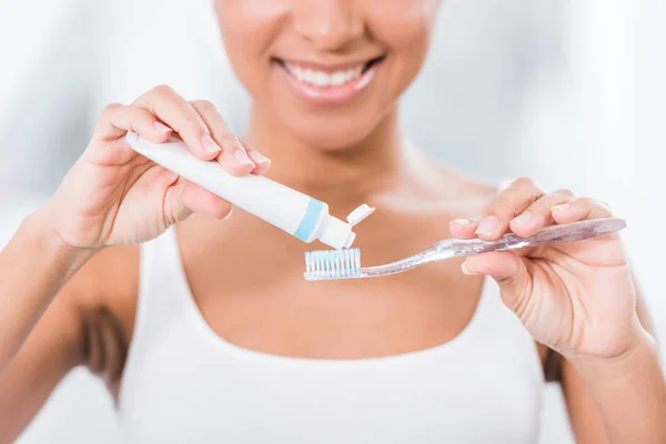Vista parcial de la mujer joven poniendo pasta de dientes en el cepillo de dientes - foto de stock